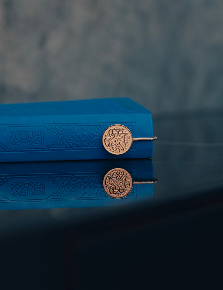 Amaani Quraan Marker clipped onto a Quran, crest sitting above the pages